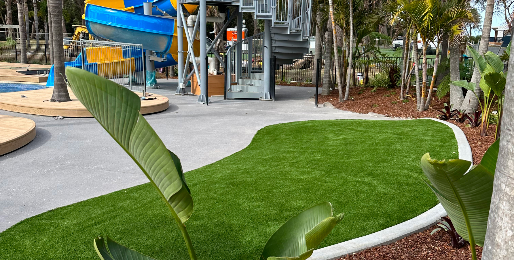 A puddle shaped turf area with a playground in the background